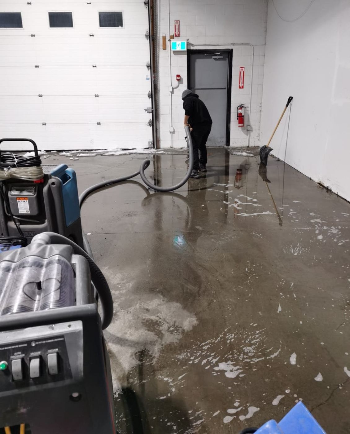 Crew extracting standing water from a warehouse floor at an overhead door during a winter flood
